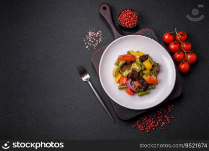 Delicious juicy fresh salad of baked eggplant, tomatoes, zucχni, onions, sπces and sa<on a dark concrete background