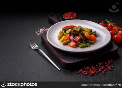 Delicious juicy fresh salad of baked eggplant, tomatoes, zucchini, onions, spices and salt on a dark concrete background