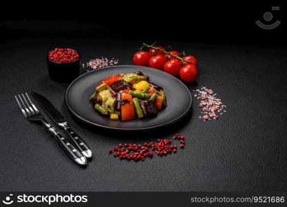 Delicious juicy fresh salad of baked eggplant, tomatoes, zucchini, onions, spices and salt on a dark concrete background