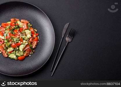 Delicious juicy fresh salad of tomatoes, peppers, cucumber, microgreens and sprouted  mung bean on a black ceramic plate on a dark concrete background