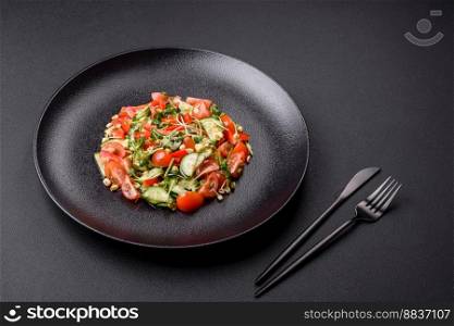 Delicious juicy fresh salad of tomatoes, peppers, cucumber, microgreens and sprouted  mung bean on a black ceramic plate on a dark concrete background