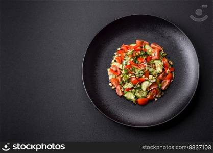 Delicious juicy fresh salad of tomatoes, peppers, cucumber, microgreens and sprouted  mung bean on a black ceramic plate on a dark concrete background