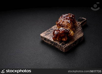 Delicious juicy fried chicken with sweet and sour teriyaki sauce and sesame seeds on a dark concrete background