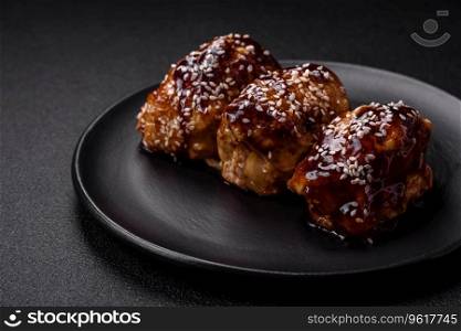 Delicious juicy fried chicken with sweet and sour teriyaki sauce and sesame seeds on a dark concrete background