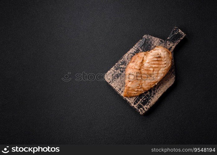 Delicious juicy grilled chicken fillet with salt, spices and herbs on a dark concrete background