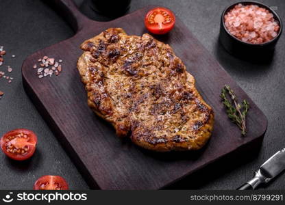 Delicious juicy grilled pork steak with spices and herbs on a wooden cutting board