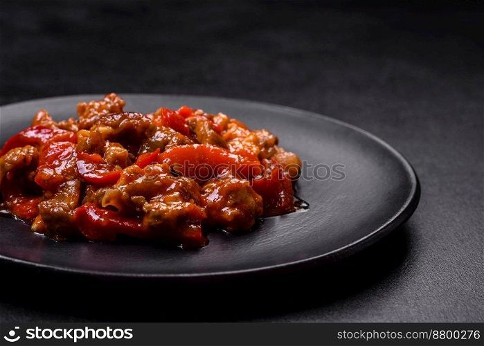 Delicious juicy meat with hot peppers and sauce on a black ceramic plate on a dark concrete background