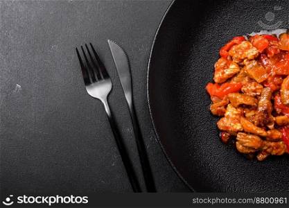 
Delicious juicy meat with hot peppers and sauce on a black ceramic plate on a dark concrete background