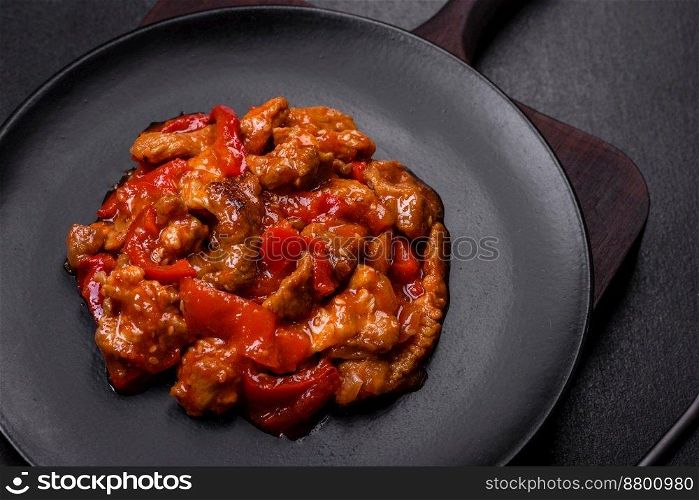  Delicious juicy meat with hot peppers and sauce on a black ceramic plate on a dark concrete background