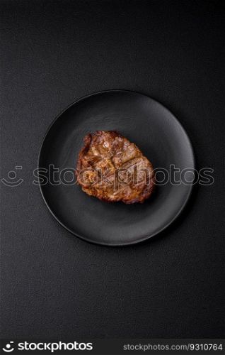 Delicious juicy pork or beef steak grilled with salt, spices and herbs on a textured concrete background