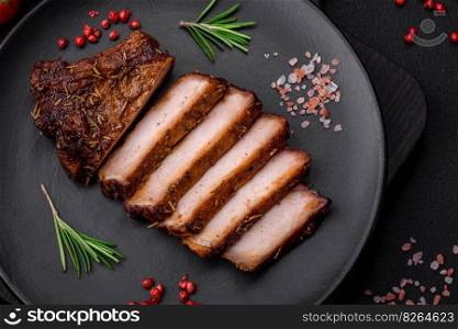 Delicious juicy pork steak on the bone with spices and herbs cut into slices on a dark concrete background
