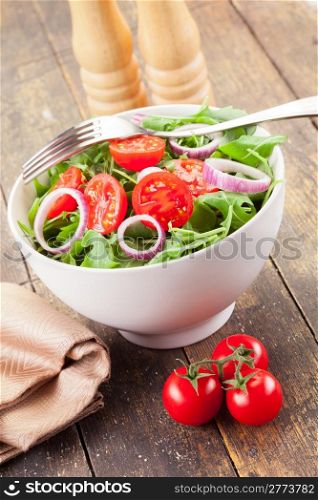 Delicious light arugula salad with tomatoes and onion rings on wooden table