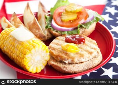 Delicious low-fat turkey burger on whole grain bun with baked potato wedges and corn. Celebrating Fourth of July by eating healthy.