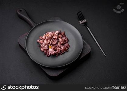 Delicious marinated octopus babies with lemon, salt and spices on a black plate on a dark concrete background