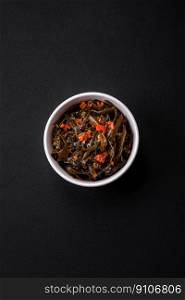 Delicious marinated seaweed with paprika, spices and salt on a dark concrete background. Delicious vegetarian salad