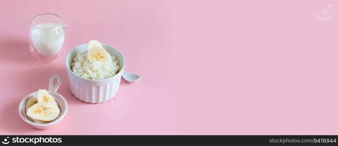 Delicious milk rice porridge with banana on a pink background with copyspace. Healthy food concept. Delicious rice milk porridge with banana on a pink background with copyspace