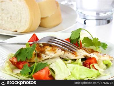 Delicious mixed salad with lettuce tomatoes and grilled chicken in white plate with silver fork.