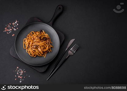 Delicious nood≤s or udon withμshrooms, sa<, sπces and herbs on a ceramic plate on a dark concrete background