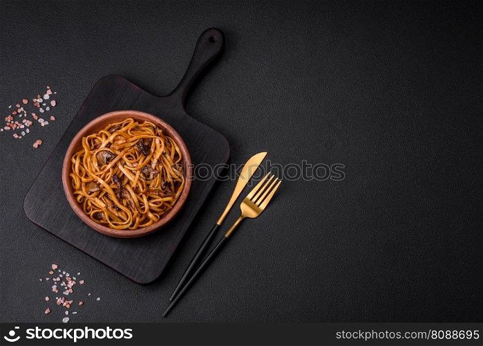 Delicious noodles or udon with mushrooms, salt, spices and herbs on a ceramic plate on a dark concrete background