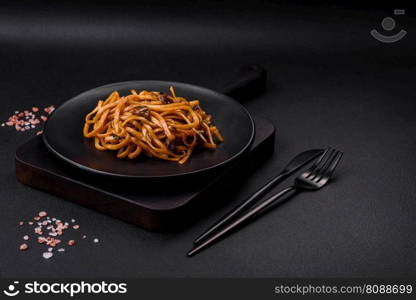Delicious noodles or udon with mushrooms, salt, spices and herbs on a ceramic plate on a dark concrete background