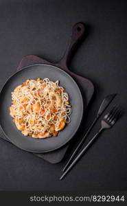 Delicious noodles with chicken and vegetables or udon on a black ceramic plate on a dark concrete background