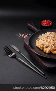 Delicious noodles with chicken and vegetables or udon on a black ceramic plate on a dark concrete background