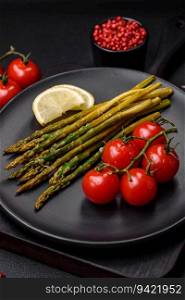 Delicious nutritious breakfast consisting of asparagus, tomatoes, salt, spices and herbs on a dark concrete background