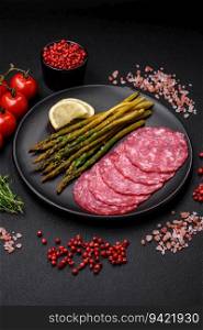 Delicious nutritious breakfast consisting of sliced sausage, asparagus, salt, spices and herbs on a dark concrete background