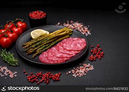 Delicious nutritious breakfast consisting of sliced sausage, asparagus, salt, spices and herbs on a dark concrete background