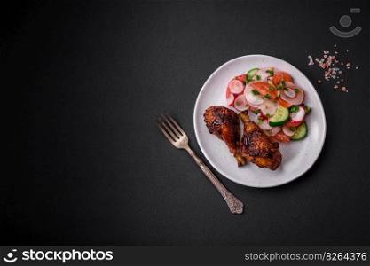 Delicious nutritious dish consisting of grilled chicken legs with a salad of tomatoes, radishes and cucumbers on a dark concrete background
