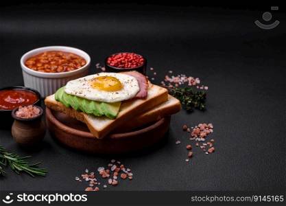 Delicious nutritious English breakfast with fried eggs, tomatoes and avocado with sπces and herbs on a dark concrete background