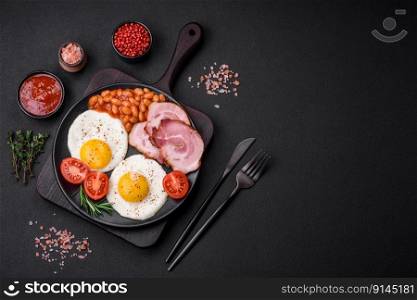 Delicious nutritious English breakfast with fried eggs, tomatoes, bacon and beans on a dark concrete background