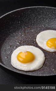 Delicious nutritious English breakfast with fried eggs, tomatoes, bacon and beans on a dark concrete background