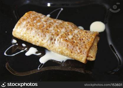 Delicious pancakes filled by fruits on black plate closeup and condensed milk over 