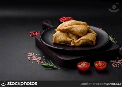 Delicious pancakes triangular shape with meat, salt and spices on a dark concrete background