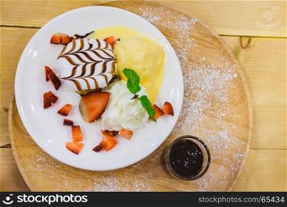 Delicious Pancakes with Strawberry and Vanilla Ice cream with chocolate topping and Whipped Cream on wooden background