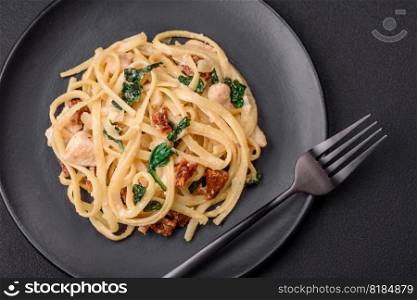 Delicious pasta with spinach, sun dried tomatoes, cheese, onions, spices and herbs on a dark concrete background