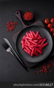 Delicious penne pasta with beets, cheese, salt and spices on a dark concrete background