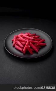 Delicious penne pasta with beets, cheese, salt and spices on a dark concrete background