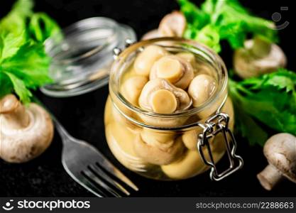 Delicious pickled mushrooms in a small glass jar on the table. On a black background. High quality photo. Delicious pickled mushrooms in a small glass jar on the table.