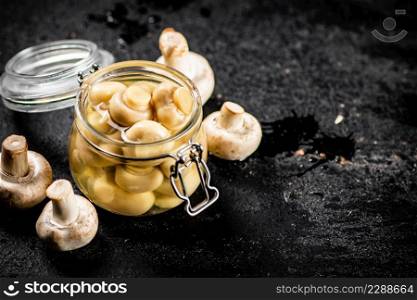 Delicious pickled mushrooms in a small glass jar on the table. On a black background. High quality photo. Delicious pickled mushrooms in a small glass jar on the table.