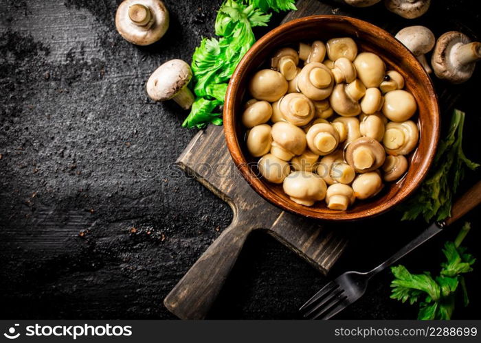 Delicious pickled mushrooms on a cutting board. On a black background. High quality photo. Delicious pickled mushrooms on a cutting board.