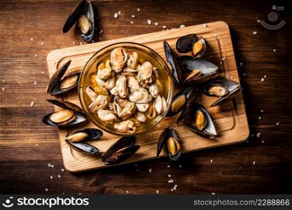 Delicious pickled mussels in a bowl on a cutting board. On a wooden background. High quality photo. Delicious pickled mussels in a bowl on a cutting board.