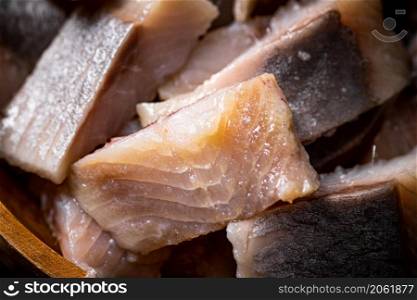 Delicious pieces of salted herring on a stone board. On a black background. High quality photo. Delicious pieces of salted herring on a stone board.