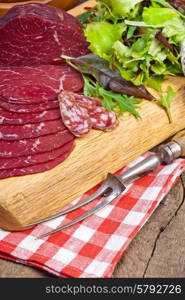 Delicious prosciutto and salami slices on wooden chopping board with vegetables and herbs. Culinary traditional ham.