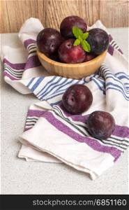 Delicious red plums in a wooden bowl on kitchen countertop.