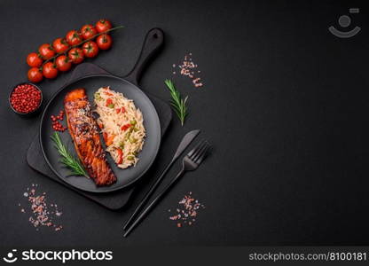 Delicious red salmon fish grilled with sauce and sesame seeds with rice, vegetables, spices and herbs on a dark concrete background