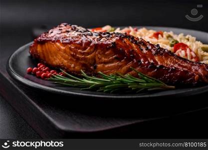 Delicious red salmon fish grilled with sauce and sesame seeds with rice, vegetables, spices and herbs on a dark concrete background