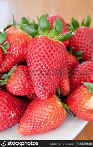 Delicious red strawberries on a white plate on a wooden table