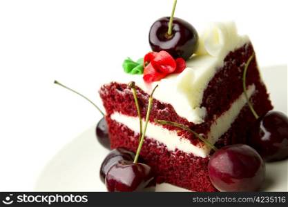 Delicious red velvet layer cake with white frosting garnished with fresh cherries against white background.